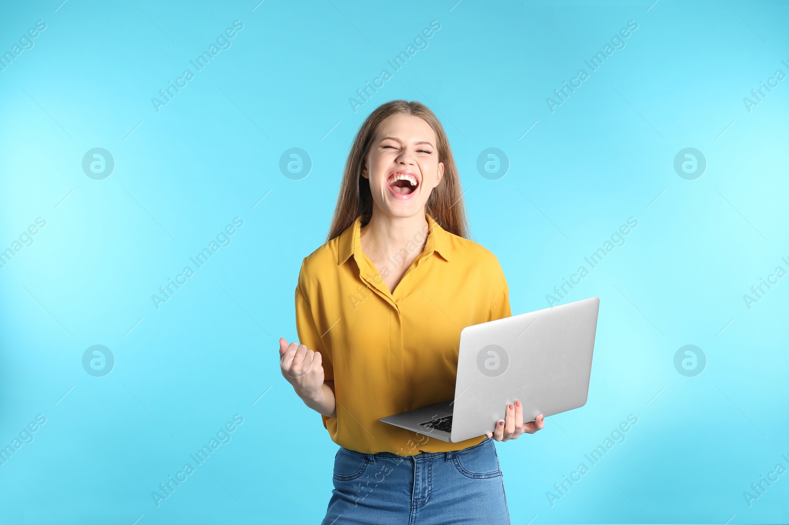 Photo of Emotional young woman with laptop celebrating victory on color background