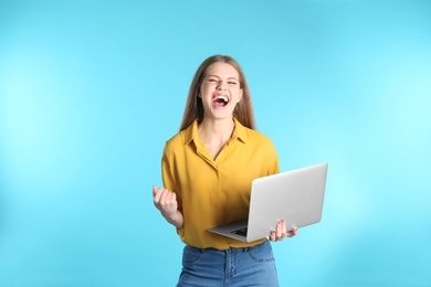 Emotional young woman with laptop celebrating victory on color background