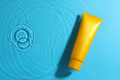 Photo of Tube with moisturizing cream in water on light blue background, top view. Space for text