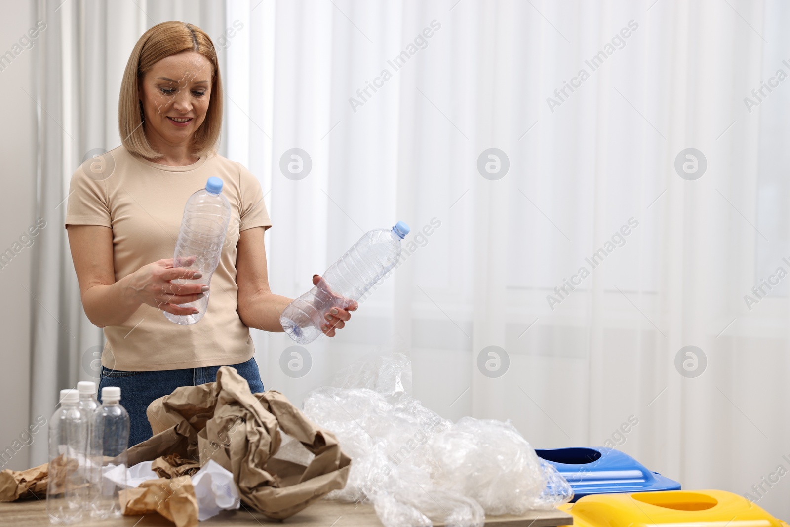 Photo of Smiling woman separating garbage in room. Space for text