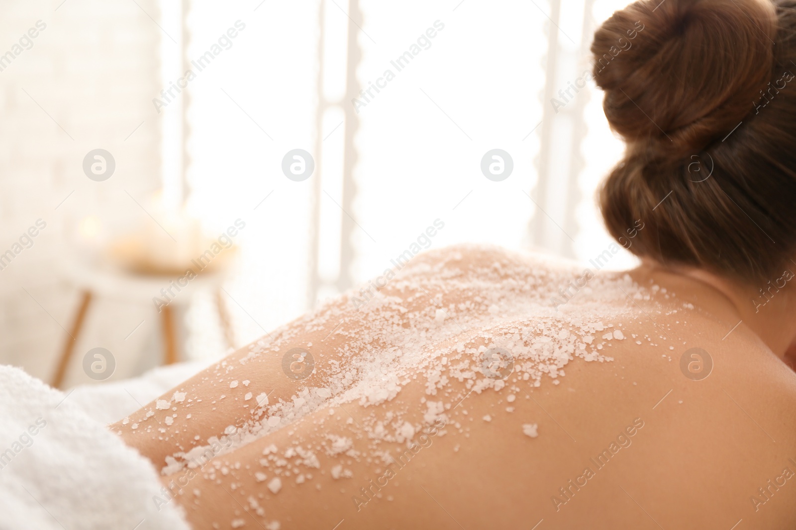 Photo of Young woman having body scrubbing procedure with sea salt in spa salon, closeup