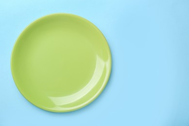 Photo of Empty green ceramic plate on light blue background, top view. Space for text