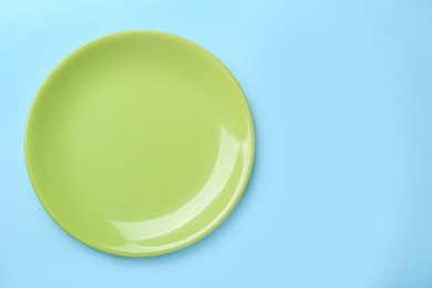 Empty green ceramic plate on light blue background, top view. Space for text