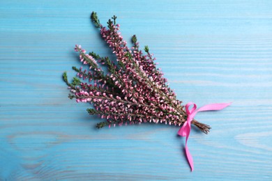 Photo of Bunch of heather branches with beautiful flowers and ribbon on light blue wooden table, top view