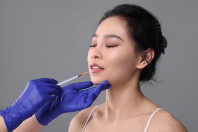 Woman getting lip injection on grey background