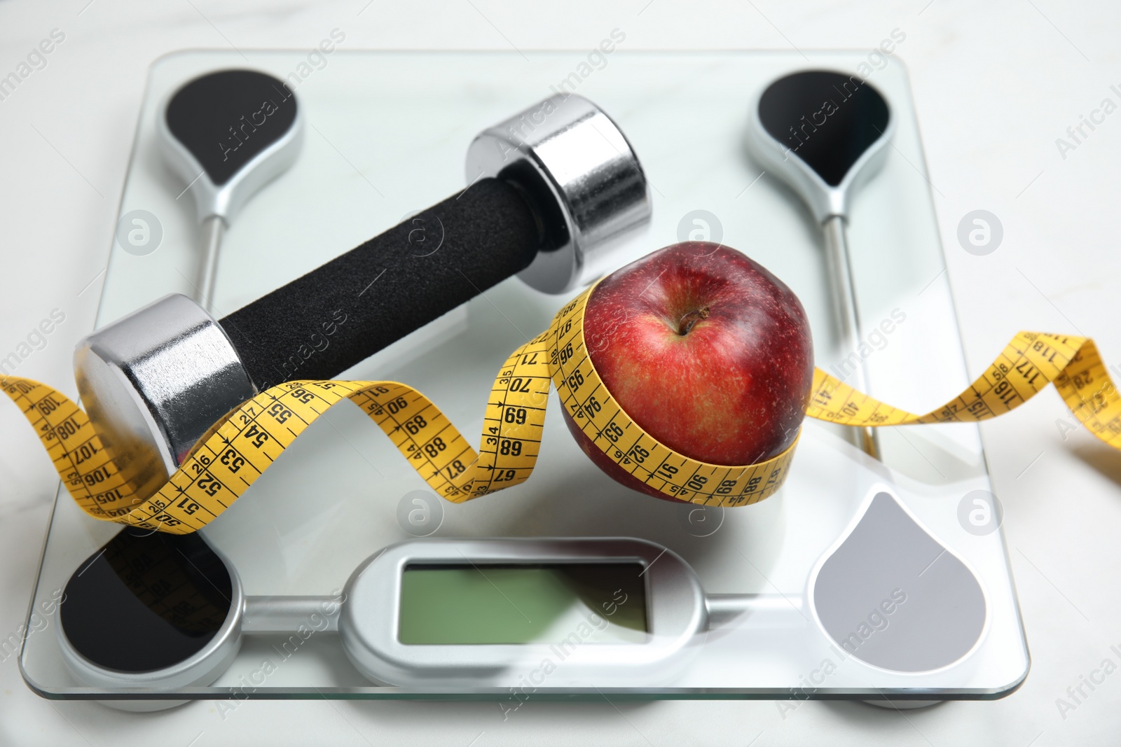 Scales, apple, measuring tape and dumbbell on white table Photo of Scales, apple, measuring tape and dumbbell on white table