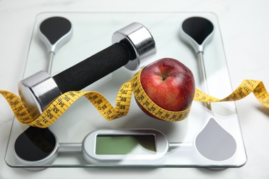 Photo of Scales, apple, measuring tape and dumbbell on white table