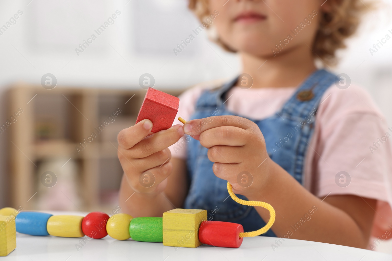 Photo of Motor skills development. Little girl playing with wooden pieces and string for threading activity at table indoors, closeup