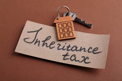 Photo of Card with phrase Inheritance Tax and key with house shaped key chain on brown background, closeup