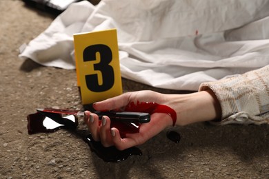 Photo of Crime scene with dead woman's body, bloody knife and marker outdoors, closeup