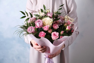 Woman with bouquet of beautiful roses on light blue background, closeup