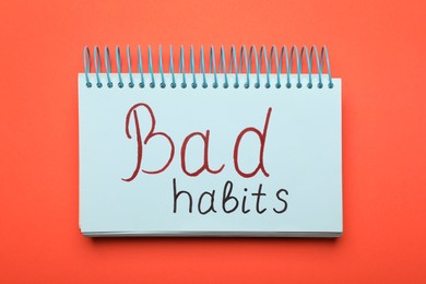 Photo of Open notebook with phrase Bad Habits on coral background, top view