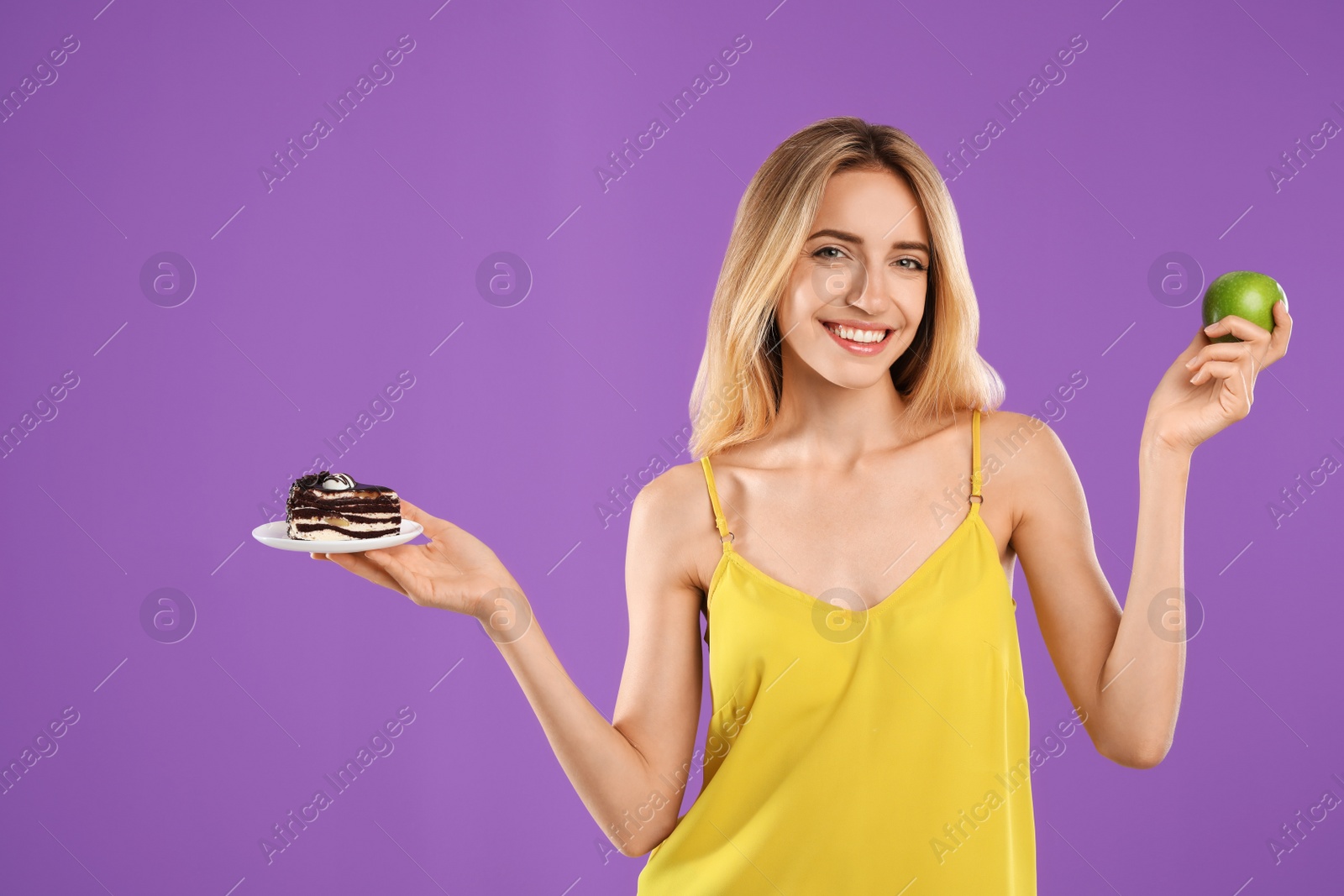 Photo of Woman choosing between cake and healthy apple on violet background