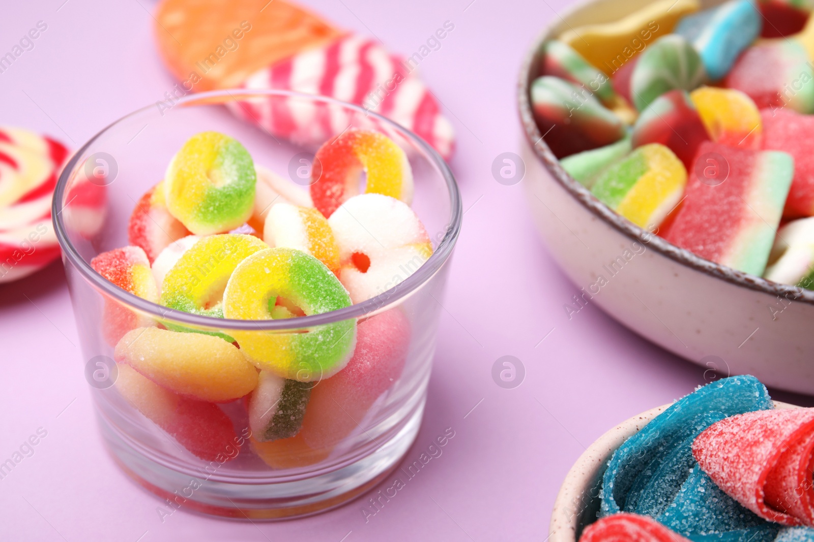 Photo of Many different jelly candies on lilac background, closeup