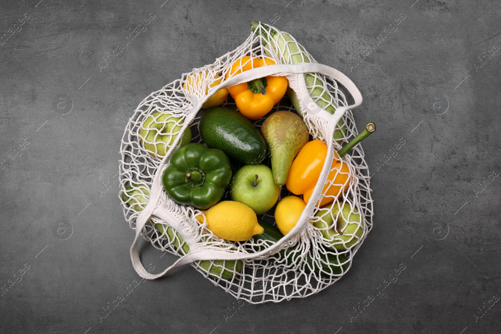 Photo of Net bag with vegetables and fruits on grey table, top view