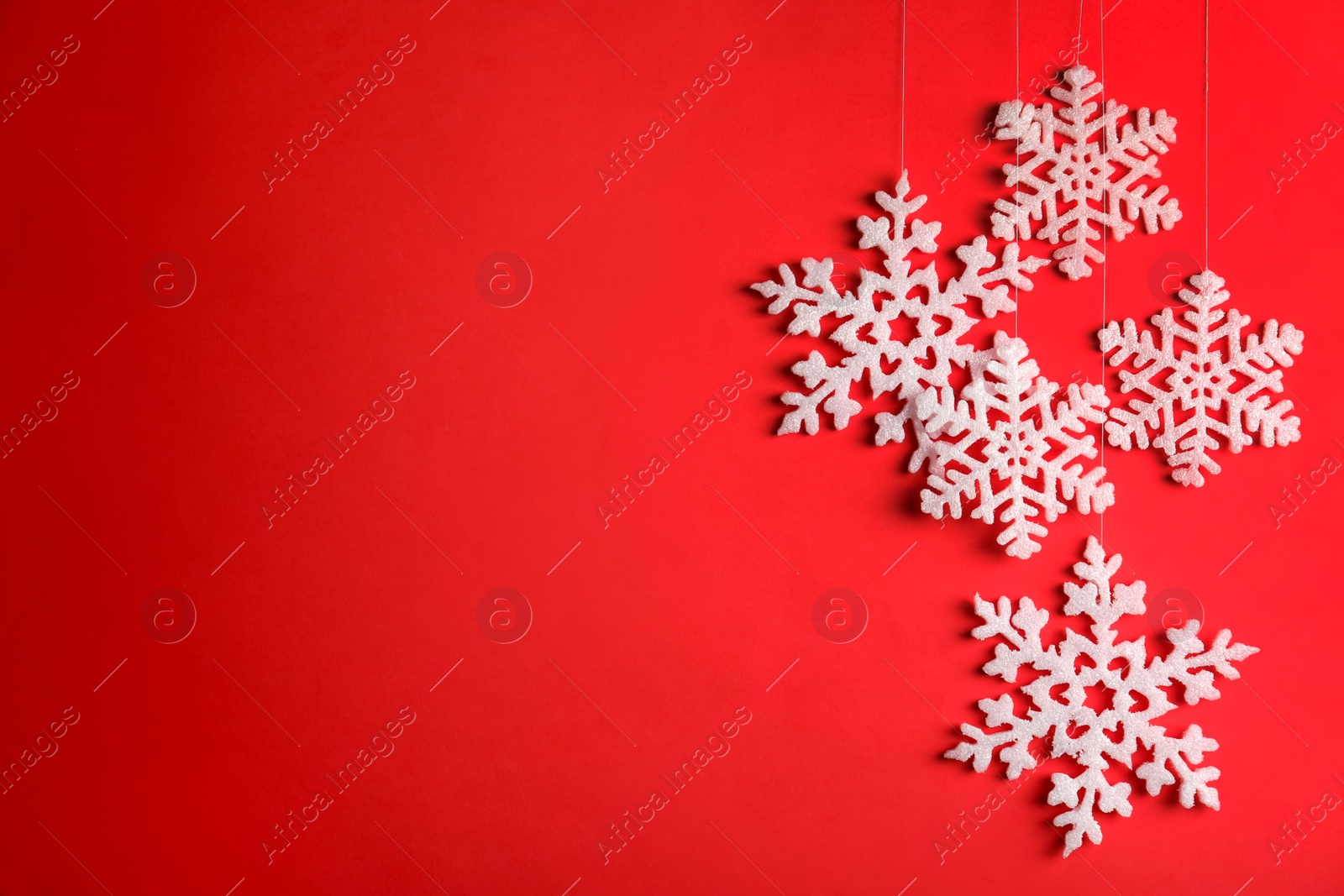 Photo of Beautiful decorative snowflakes hanging on red background, space for text