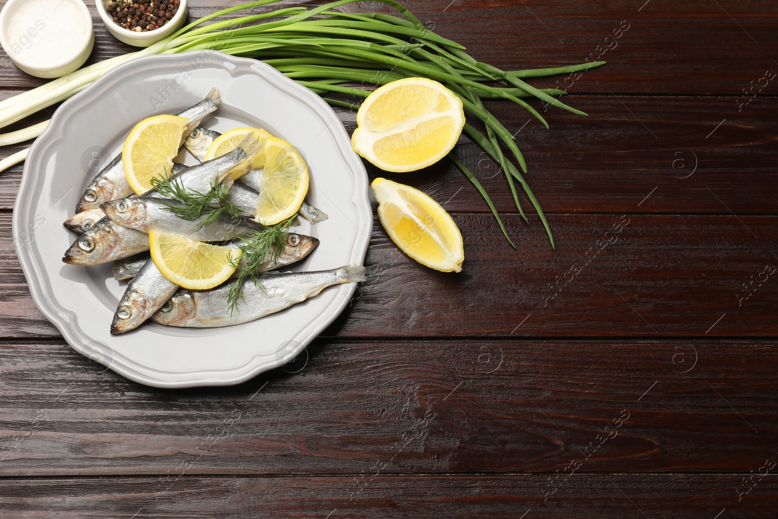 Photo of Fresh raw sprats, onion, cut lemon and spices on wooden table, flat lay. Space for text