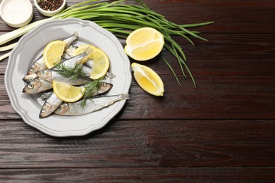 Fresh raw sprats, onion, cut lemon and spices on wooden table, flat lay. Space for text