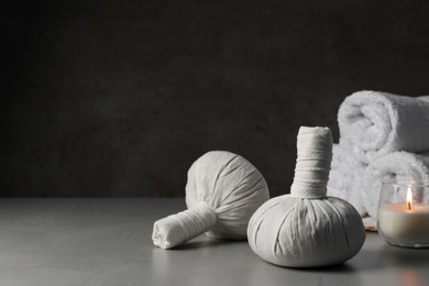 Photo of Herbal massage bags, candle and rolled towels on grey table, space for text. Spa supply