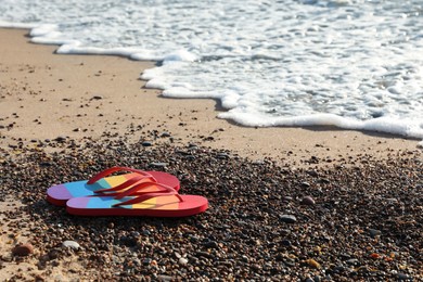 Stylish rainbow flip flops on pebbles near sea. Space for text