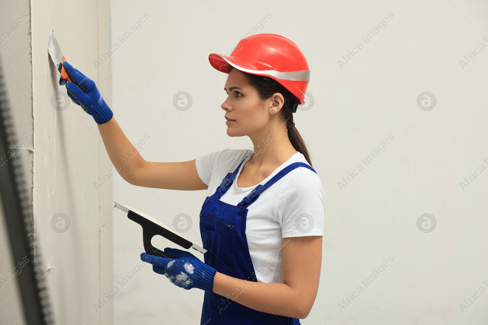 Photo of Professional worker in hard hat plastering wall with putty knives, closeup