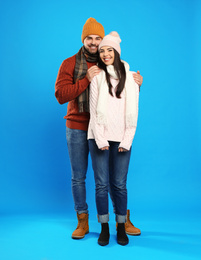 Happy young couple in warm clothes on blue background. Winter vacation