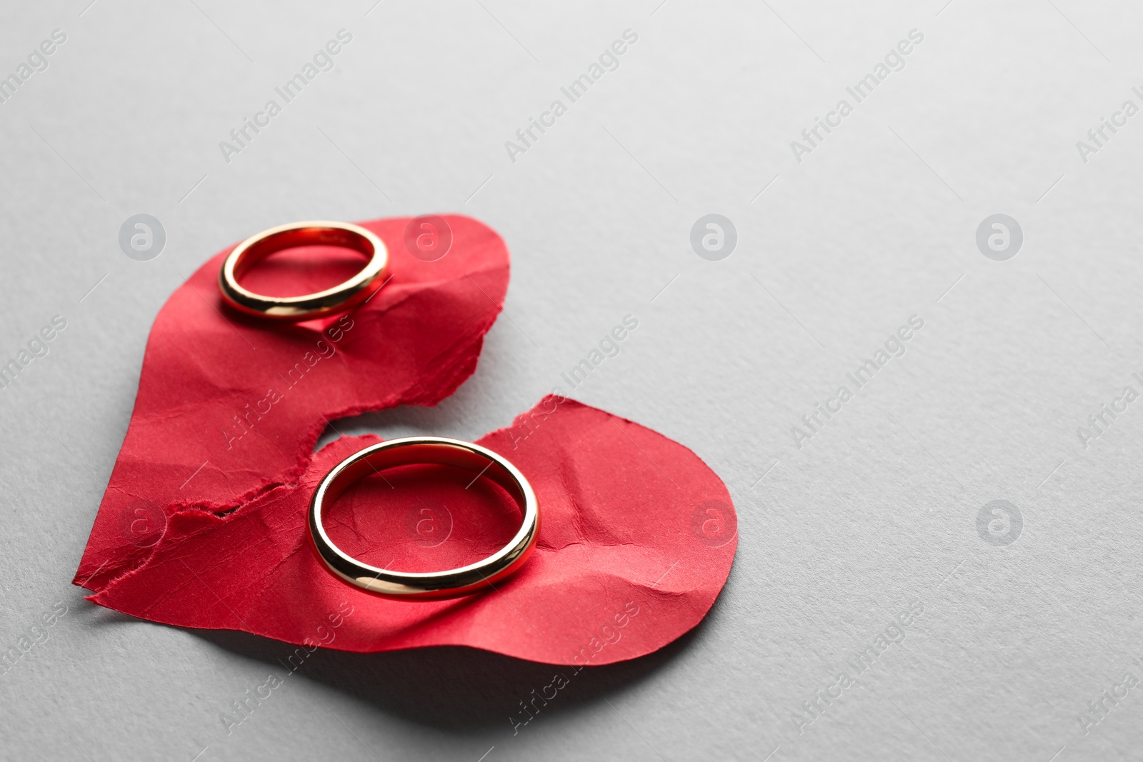 Photo of Halves of torn red paper heart and wedding rings on white background, space for text. Broken heart