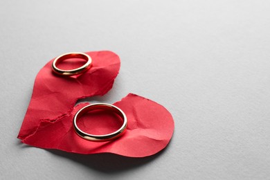 Halves of torn red paper heart and wedding rings on white background, space for text. Broken heart