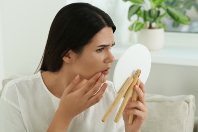 Young woman looking in mirror on her pimples indoors. Hormonal disorders