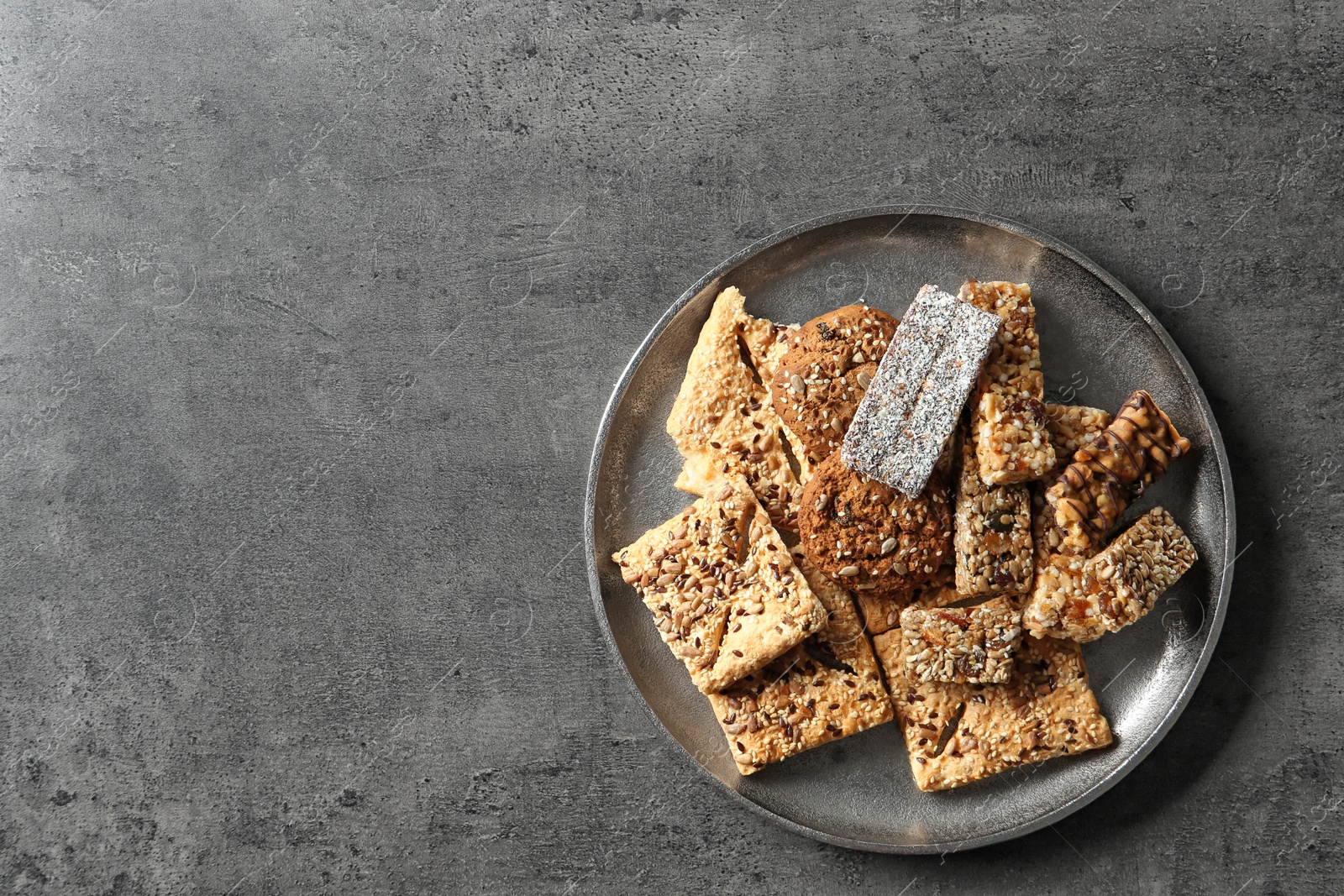 Photo of Plate with cookies and cereal bars on grey background, top view. Whole grain snack