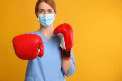 Photo of Doctor with protective mask and boxing gloves on yellow background, space for text. Strong immunity concept