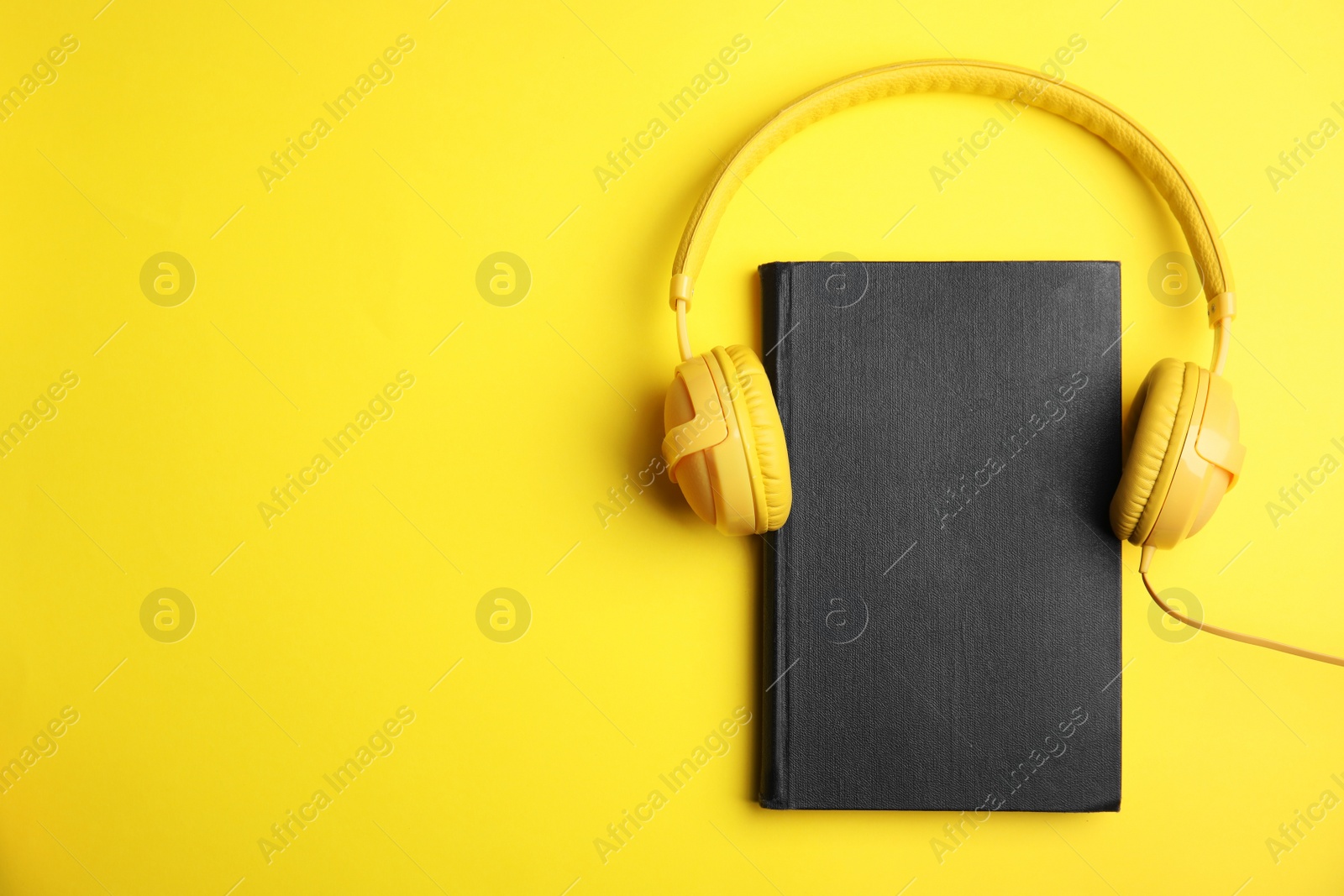 Photo of Book and modern headphones on yellow background, top view. Space for text