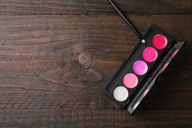 Photo of Colorful lipstick palette and brush on wooden table, flat lay with space for text. Professional cosmetics