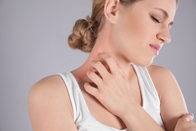 Woman scratching neck on grey background. Allergy symptoms