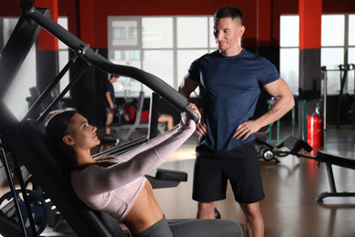 Trainer with young woman working out on chest press machine in gym