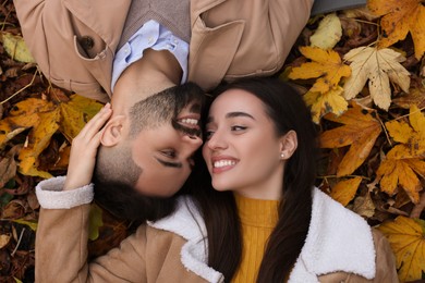 Happy young couple lying on dry leaves outdoors, top view