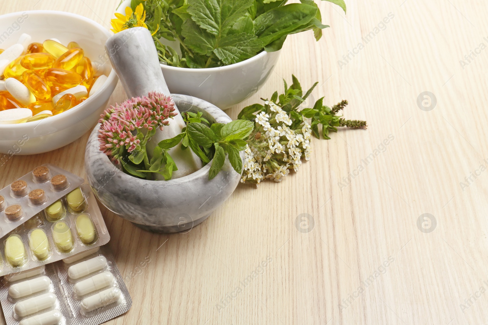 Photo of Mortar with fresh herbs and pills on wooden table, space for text