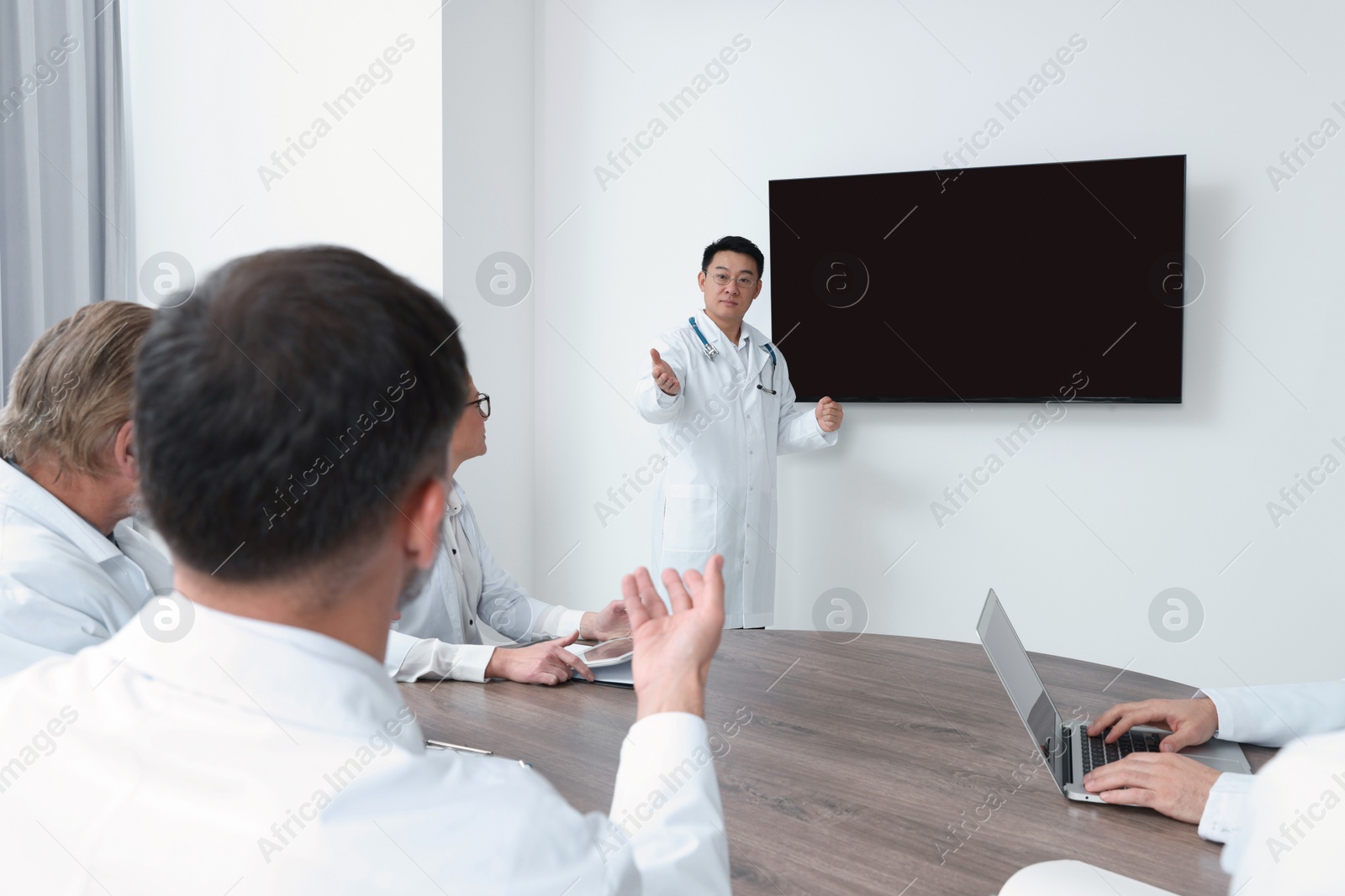 Photo of Team of doctors listening to speaker report near tv screen in meeting room. Medical conference