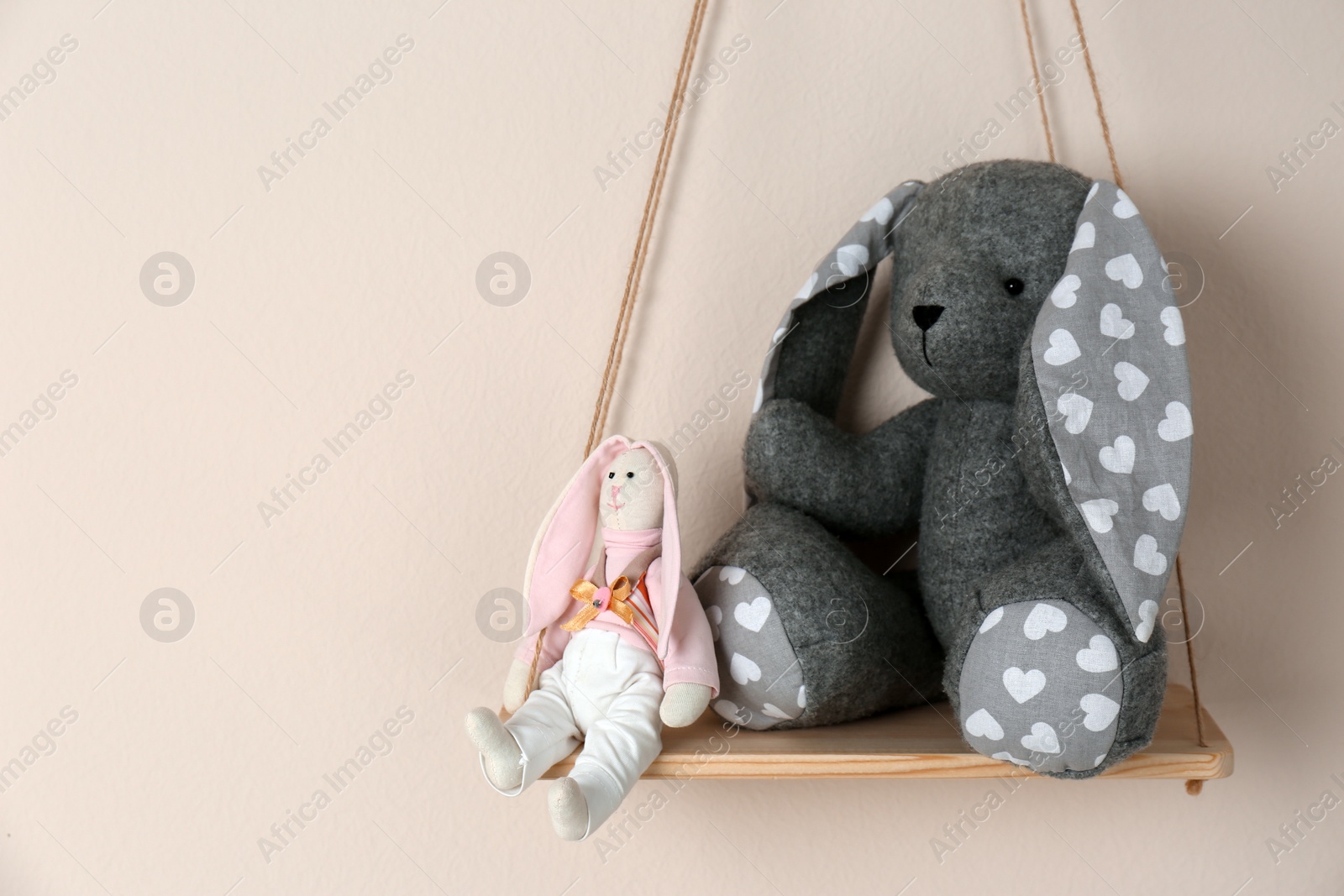 Photo of Shelf with cute toy bunnies on beige wall, space for text. Child's room interior element