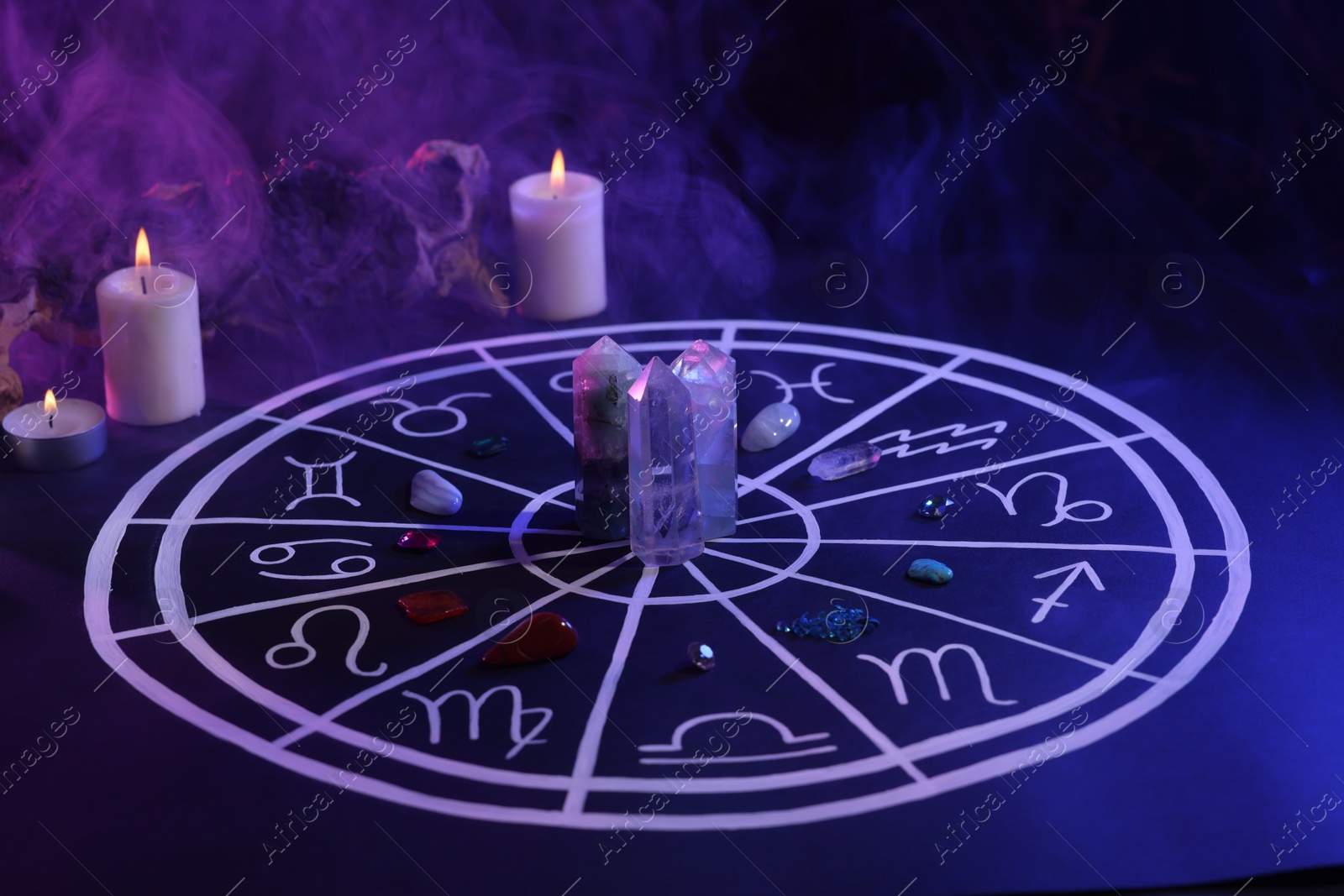 Photo of Natural stones for zodiac signs, drawn astrology chart and burning candles on dark blue table. Color tone effect