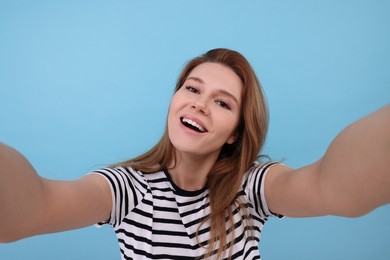Beautiful woman taking selfie on light blue background