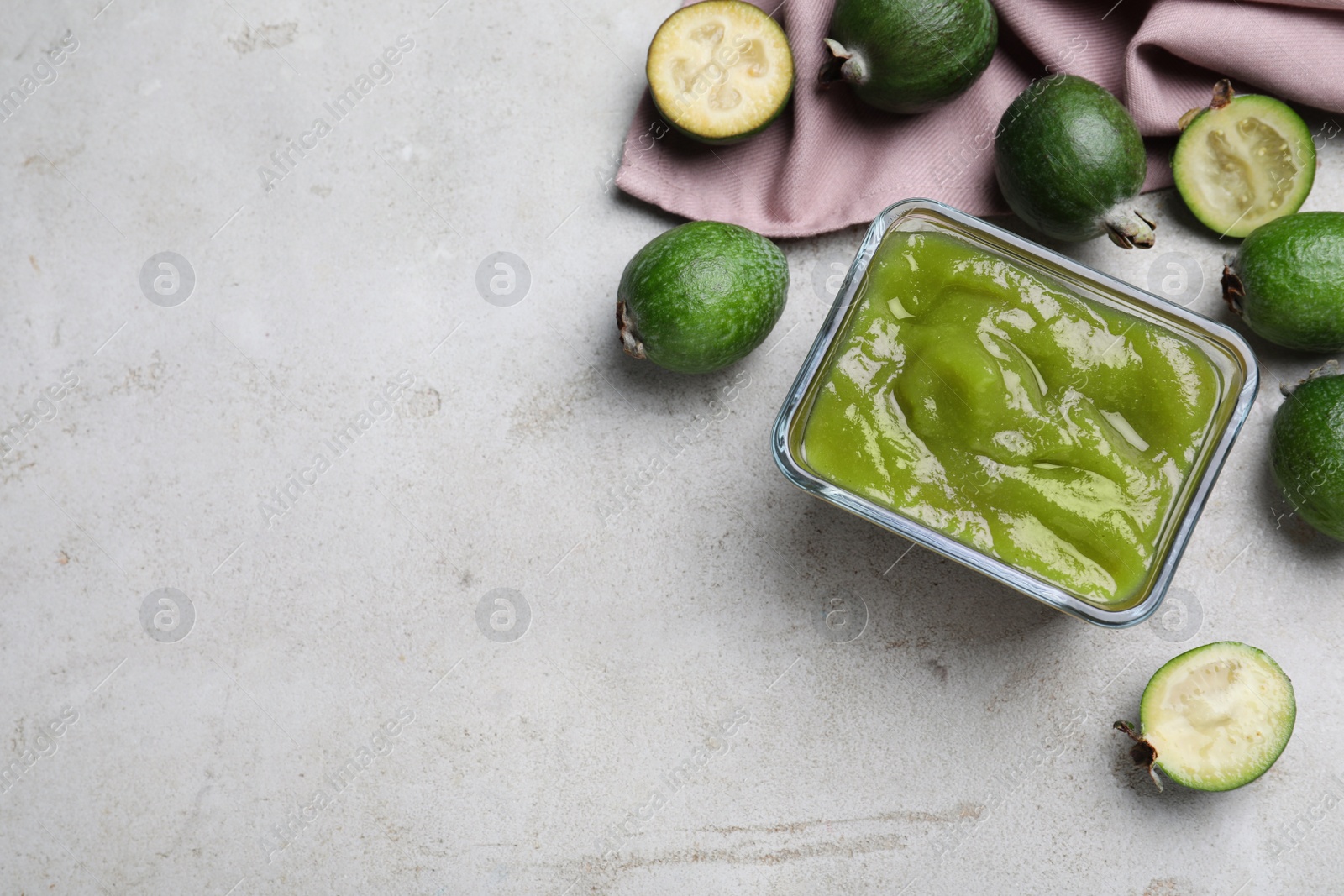 Photo of Feijoa jam and fresh fruits on light grey table, flat lay. Space for text