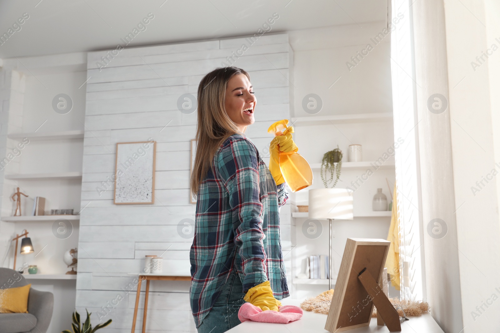 Photo of Woman with spray bottle and rag singing while cleaning at home