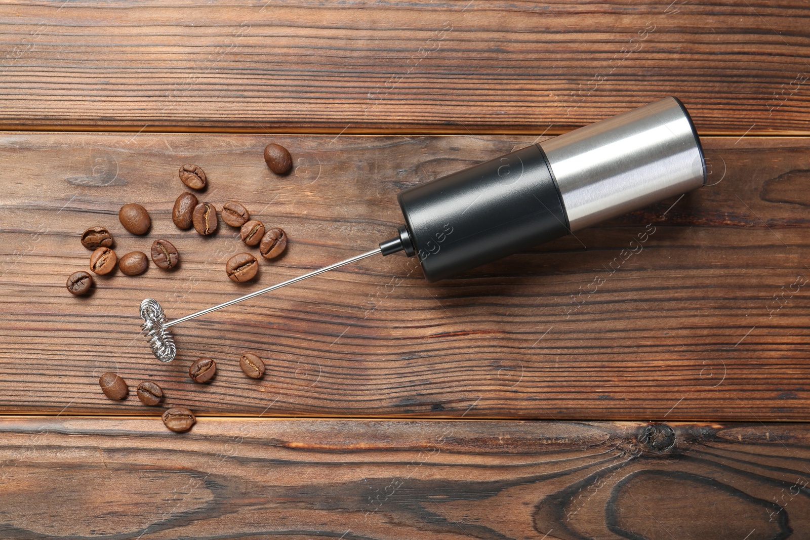 Photo of Black milk frother wand and coffee beans on wooden table, top view