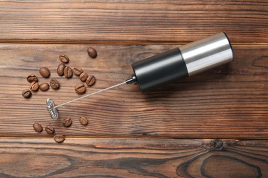 Black milk frother wand and coffee beans on wooden table, top view