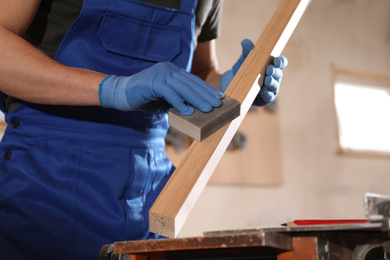 Photo of Professional carpenter polishing wooden bar in workshop, closeup