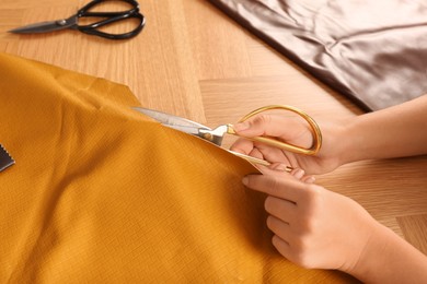 Photo of Woman cutting orange leather with scissors at wooden table, closeup