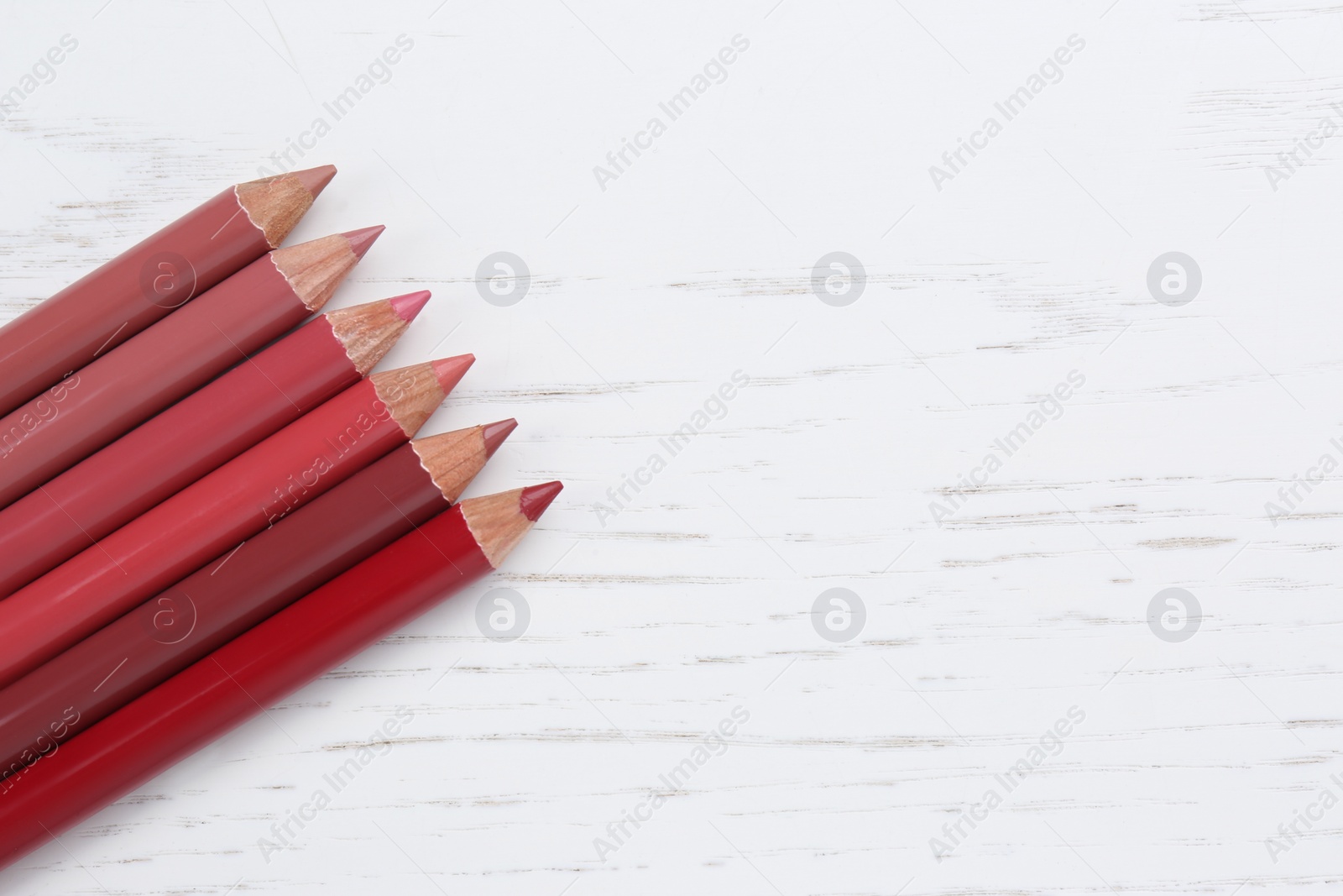 Photo of Different lip pencils on white wooden table, flat lay with space for text. Cosmetic product