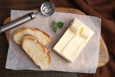 Photo of Tasty butter, slices of bread and spoon on wooden table, top view