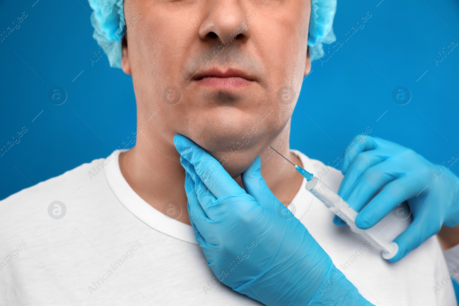 Photo of Mature man with double chin receiving injection on blue background, closeup